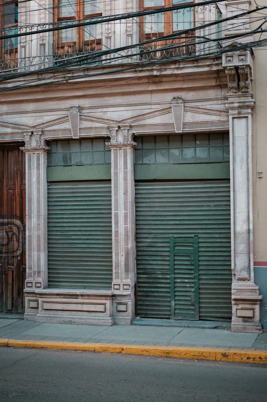 A closed storefront with green metal shutters on a quiet street