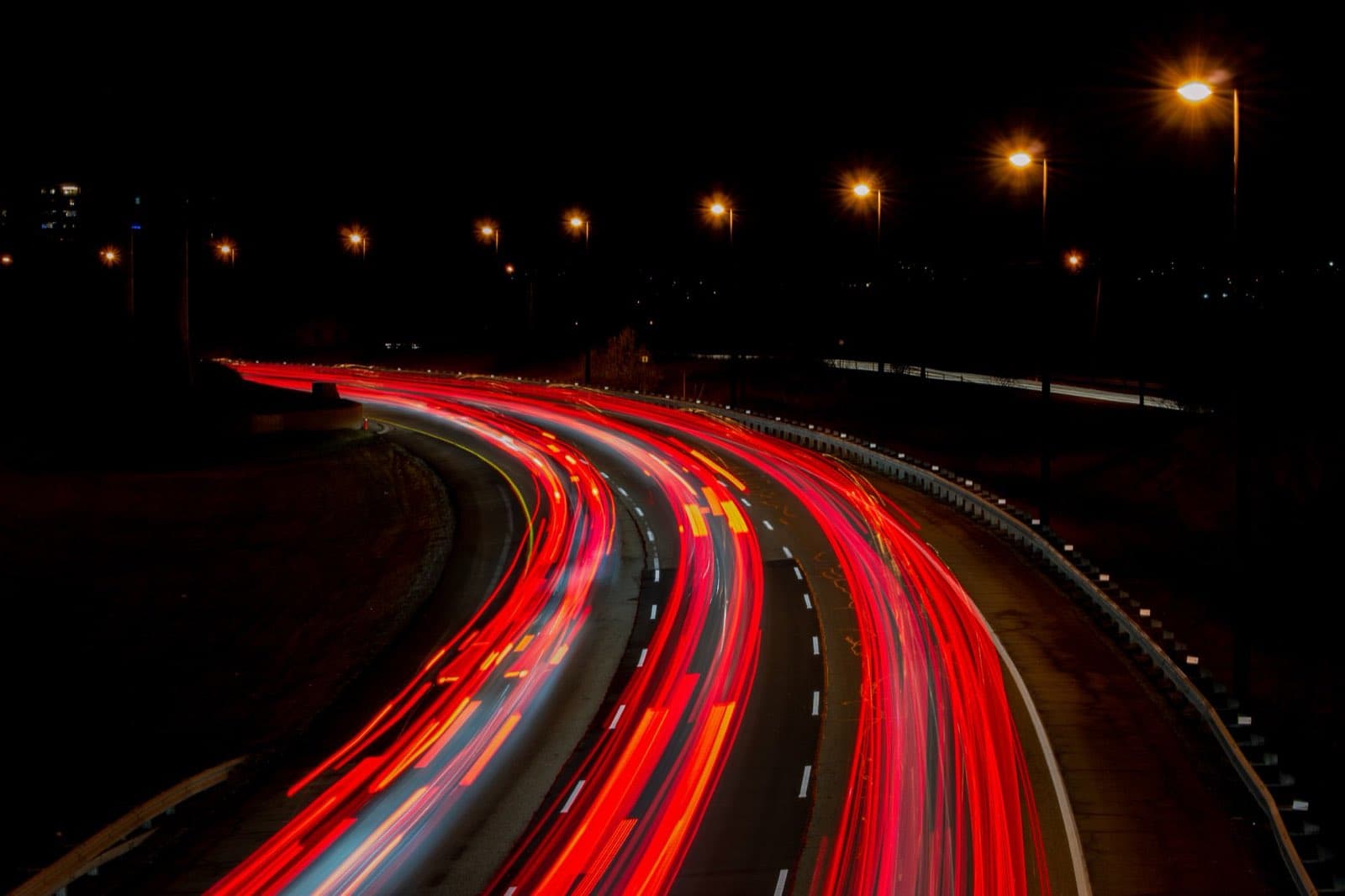 Red tail-light trails curving along a highway at night