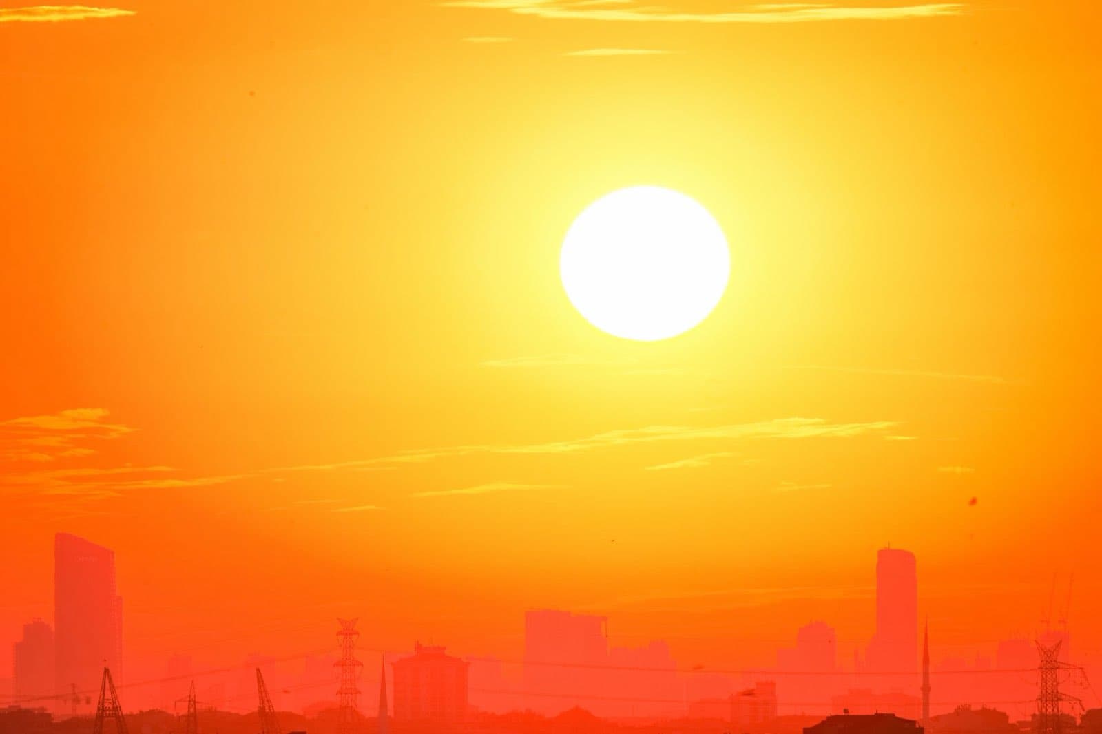 A huge sun over a hazy city skyline, the whole frame washed in orange heat