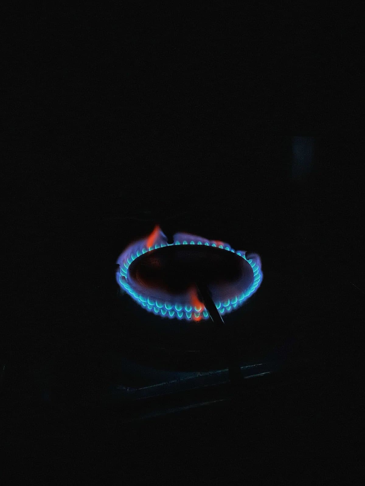 A gas stove burner ring burning blue in a dark kitchen