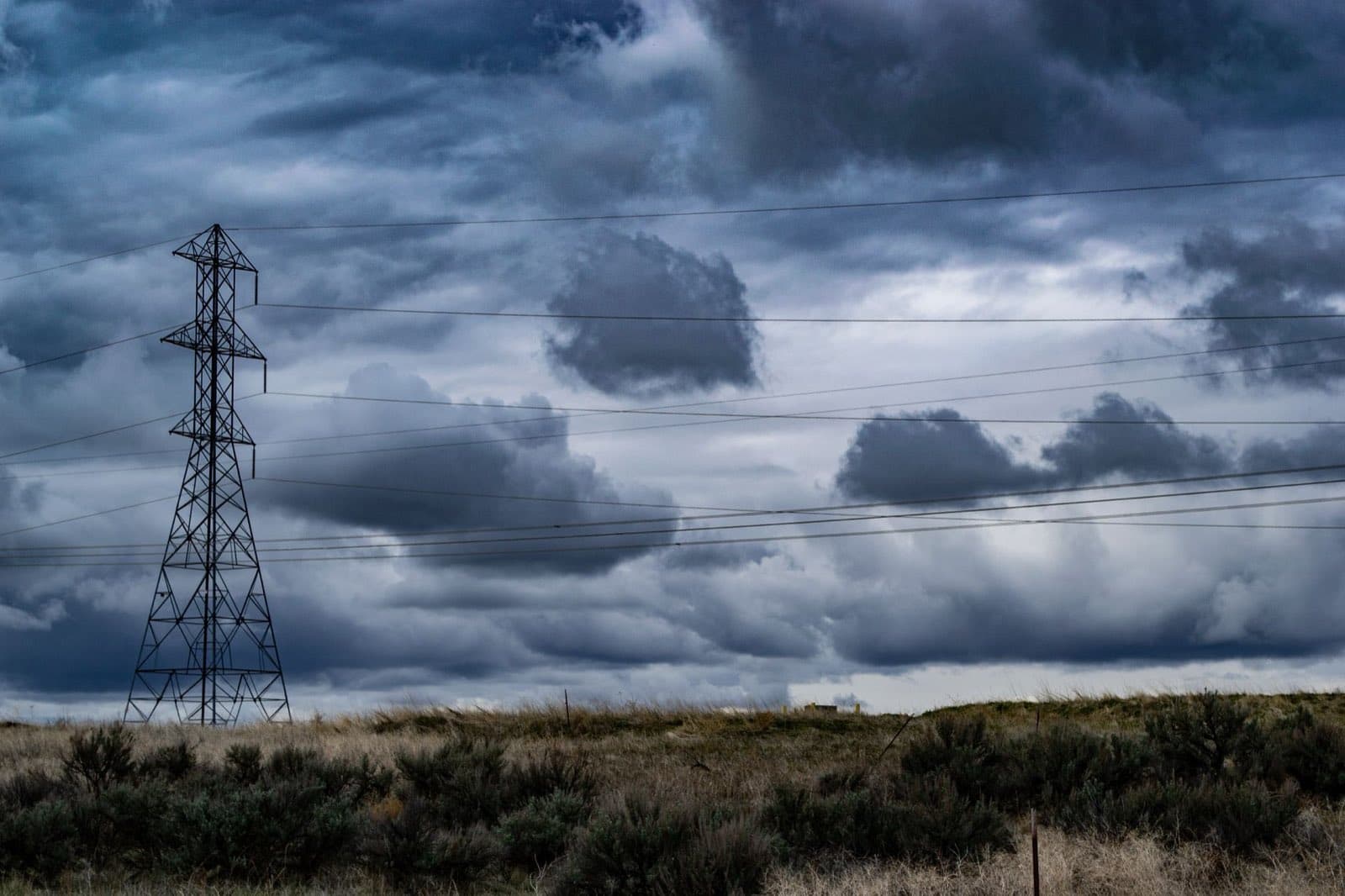 A transmission tower in a field under heavy storm clouds