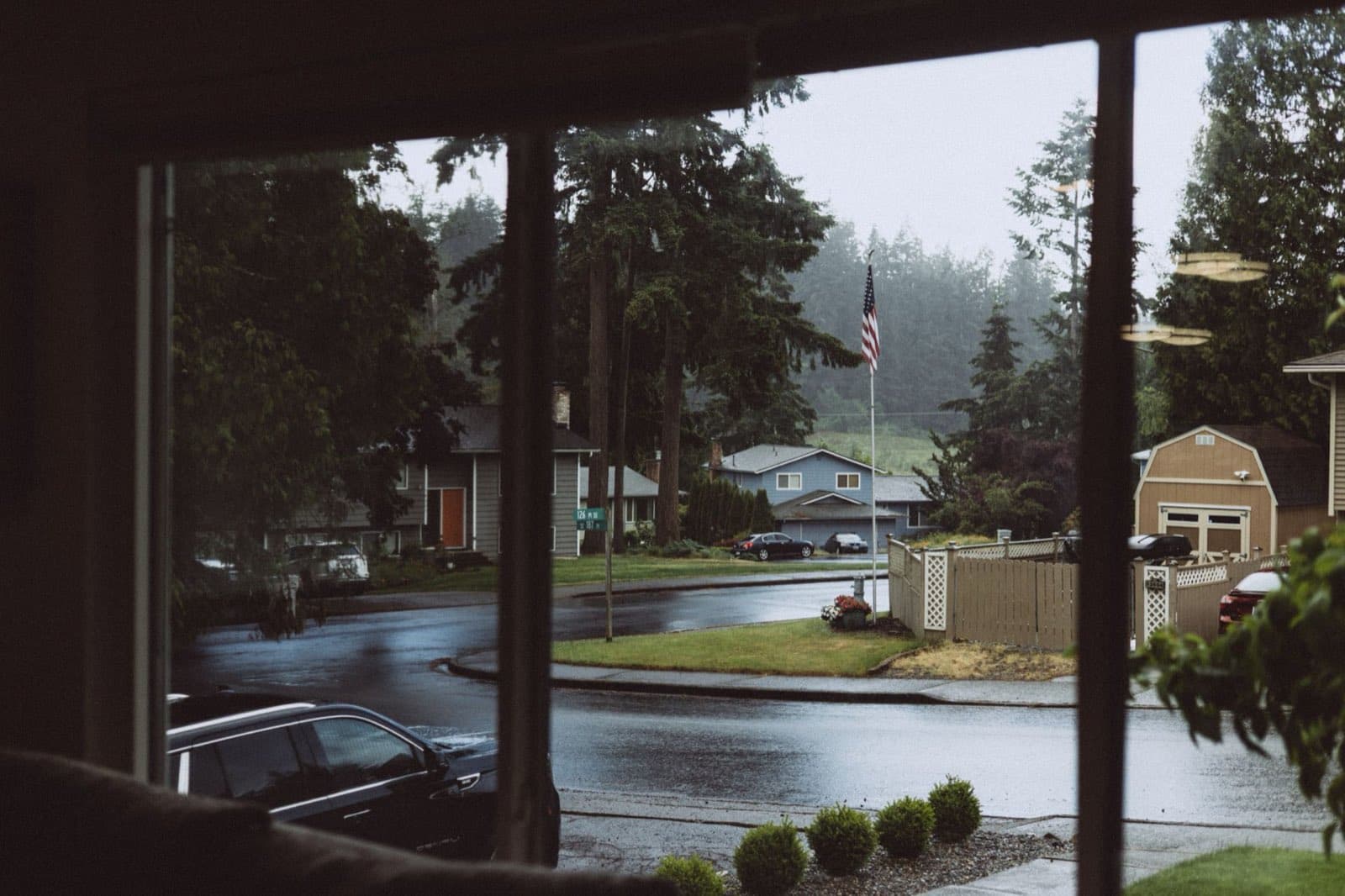 A rainy suburban street seen from inside through a living room window