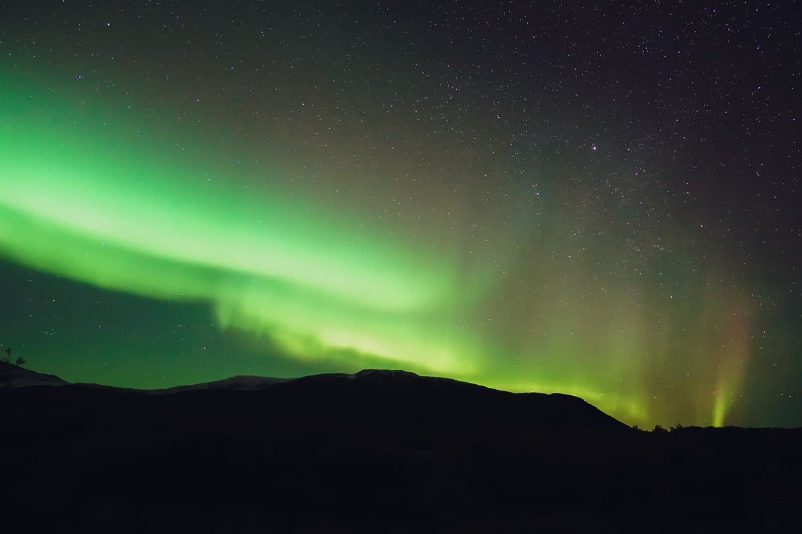 Green aurora borealis rippling over a dark mountain ridge under a starry sky